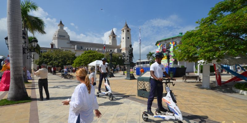 tourists pass by as police rides a modern scooter in the park